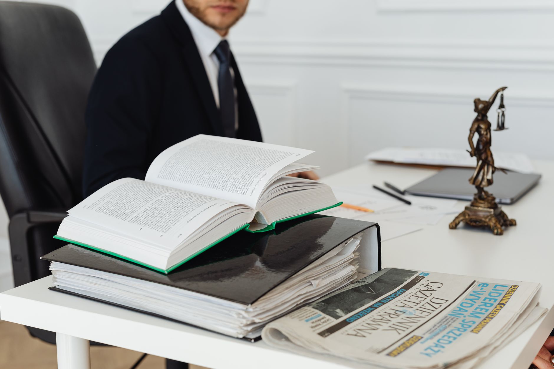 Rechtsanwalt im Gespräch mit Gesetzbüchern und Justitia-Figur auf dem Schreibtisch